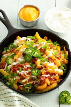 a skillet filled with pasta and vegetables on top of a white table next to green peppers