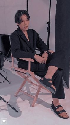 a woman sitting in a chair with her legs crossed and shoes on the ground behind her