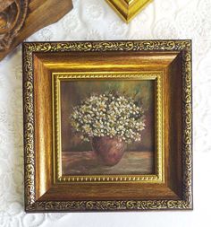 an oil painting of daisies in a gold frame on a white tablecloth next to other items