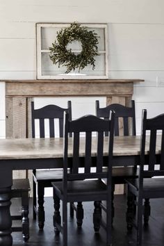 a dining room table with black chairs and a wreath on the fireplace mantel above it