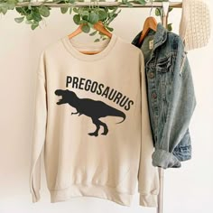 a dinosaur sweatshirt hanging on a rack next to a pair of denim jackets and jeans