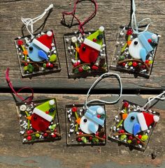 four glass ornaments are sitting on a wooden surface, each decorated in different colors and shapes