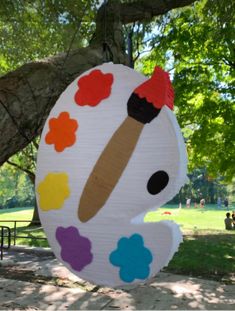 a paper plate shaped like an artist's palette hanging from a tree in a park