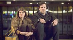 a man and woman sitting next to each other in front of a gate at night