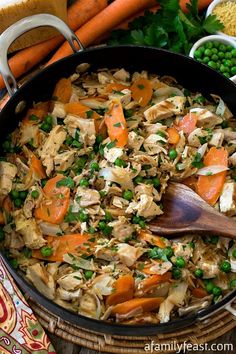 a pan filled with vegetables and meat on top of a wooden table next to peas