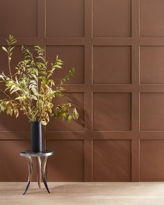 a plant in a vase sitting on a table next to a wall with brown tiles