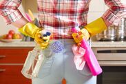 a woman standing in a kitchen holding two pink and yellow utensils on her hip