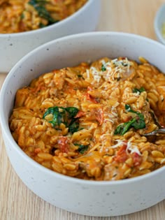 two white bowls filled with pasta and spinach on top of a wooden table,