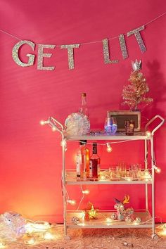 a bar cart with bottles and glasses on it in front of a pink wall that says get lit