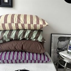 a stack of pillows sitting on top of a bed next to a table with an alarm clock