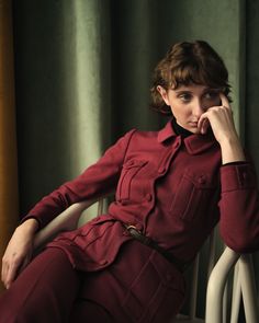 a woman is sitting in a chair with her hand on her chin and looking at the camera