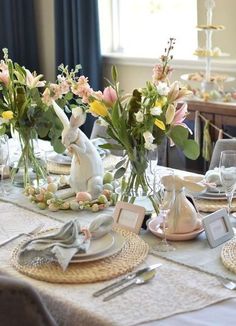 the table is set for easter dinner with bunny figurines and flowers in vases