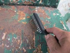 a person holding a brush on top of a rusted green bench with peeling paint