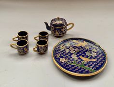 a blue and gold tea set with matching cups, saucers and spoons on a white table