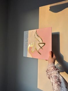 a person holding up a piece of paper with gold foil on it in front of a wall