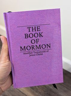 a person holding up a purple book with the title, the book of mormon written on it