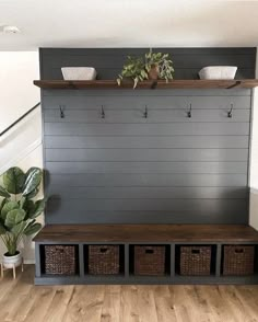 a wooden bench with baskets on it in front of a wall mounted coat rack and potted plants