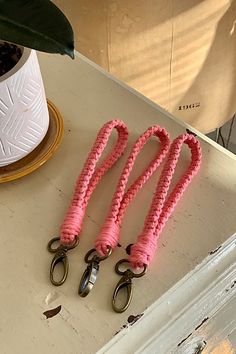 three pairs of pink roped scissors sitting on top of a white table next to a potted plant