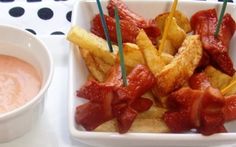 a white plate topped with french fries covered in ketchup next to a bowl of dip