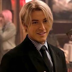 a man with blonde hair wearing a black suit and striped shirt smiling at the camera