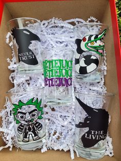 six shot glasses in a cardboard box with halloween stickers on the lids and sides