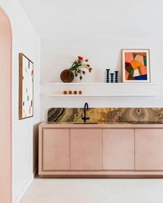 a modern kitchen with pink cabinets and artwork on the wall above it's sink