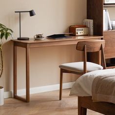 a bedroom with a bed, desk and chair next to a plant in the corner