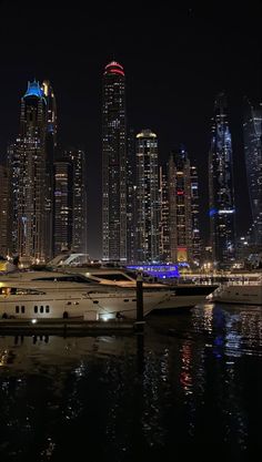 a large white boat floating in the water next to a city at night with lights on