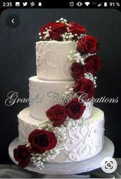 a wedding cake decorated with red roses and baby's breath