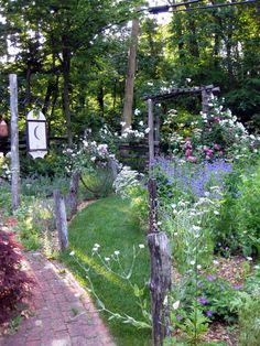 the garden is full of flowers, plants and an old wooden trellis with a clock on it