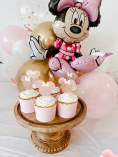 a minnie mouse cake and cupcakes on a table with balloons in the background