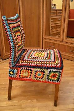 a colorful crocheted chair sits in front of a wooden dresser with drawers and mirror