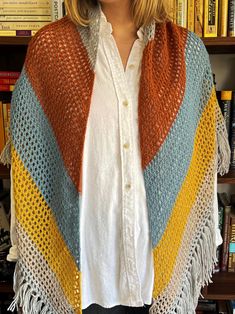 a woman standing in front of a bookshelf wearing a multicolored shawl