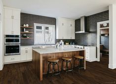 a large kitchen with white cabinets and wooden flooring is pictured in this image, there are three stools at the center of the island