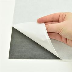 a hand holding a piece of white paper on top of a sheet of gray fabric