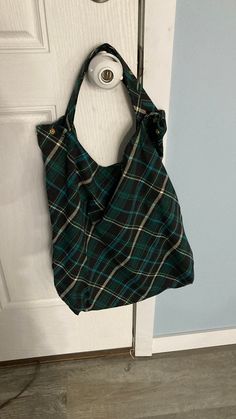 a green and black plaid purse hanging on a door handle next to a white door