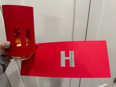 a person holding up a red paper with the letter h on it