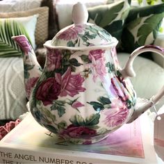 a teapot sitting on top of a book next to a couch with pillows in the background