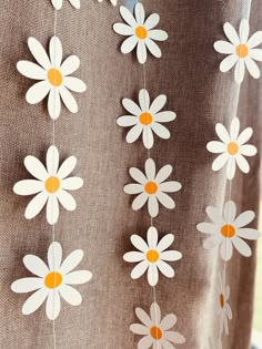 white and orange flowers are hanging from the side of a curtain with yellow centers on it