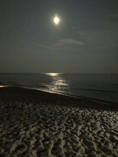 the moon is shining over the ocean on a beach