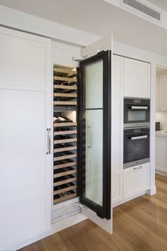 an empty wine cooler in the middle of a kitchen with white cabinets and wood floors