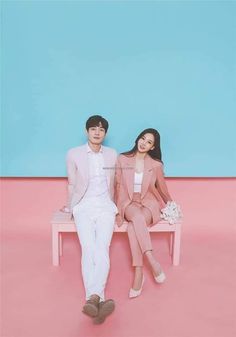 two people sitting on a bench in front of a blue and pink wall