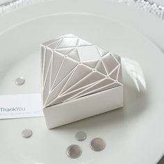 a white plate topped with an origami shaped box next to small silver discs