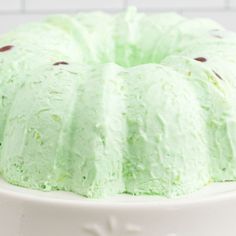 a cake with green frosting sitting on top of a white plate in front of a brick wall