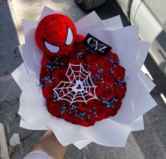 a spiderman cake on top of white paper with blue sprinkles and red roses