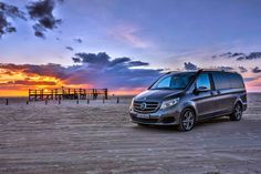 a van parked on the beach at sunset with clouds in the sky and pier in the background