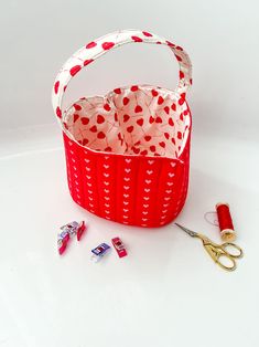 a red basket with hearts on it next to scissors and pins