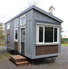 a tiny house sitting on top of a gravel lot next to a wooden step leading up to it