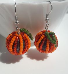 two orange and green beaded pumpkins are hanging from silver earwires on a white plate