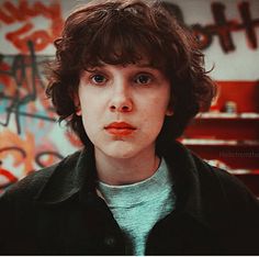 a young man in a black jacket looking at the camera with graffiti on the wall behind him